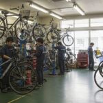 自転車がたくさんあり、つなぎを着た整備士が自転車を修理している